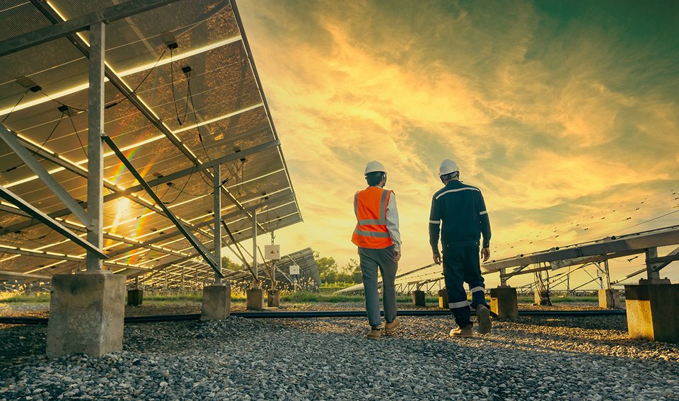 Two workers walking along a series of panels in a field, low perspective, sunrise or sunset