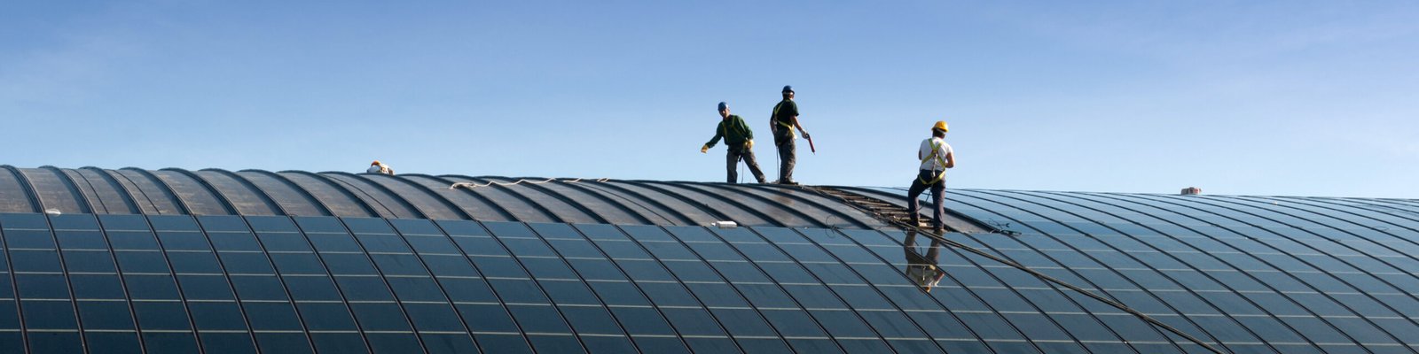Workers on a large curved roof installing solar panels