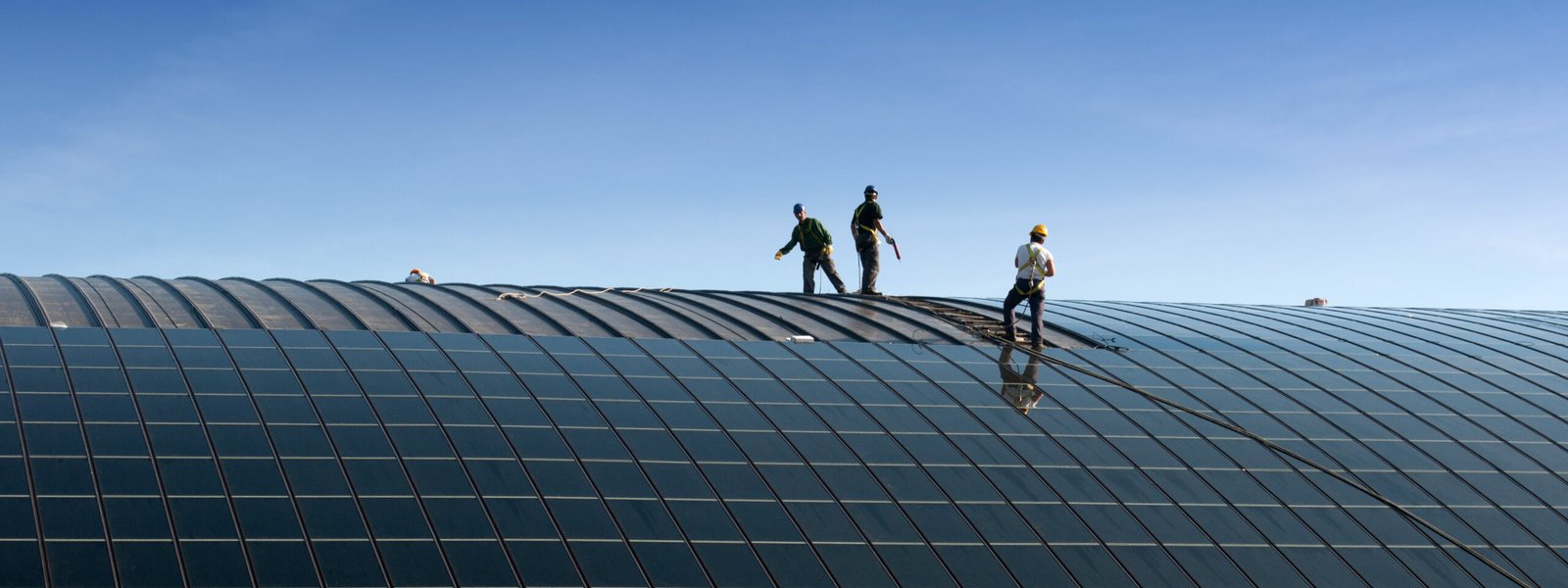 Workers on a large curved roof installing solar panels