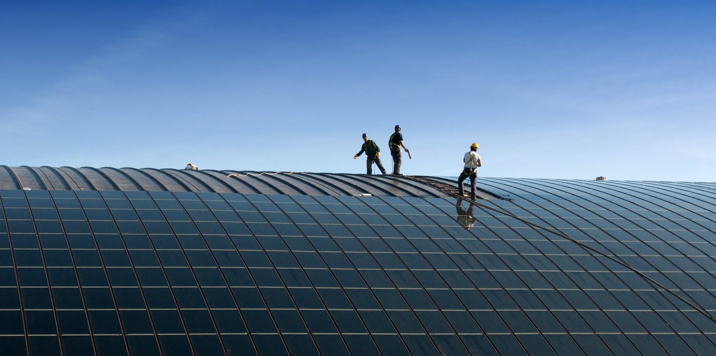 Workers on a large curved roof installing solar panels