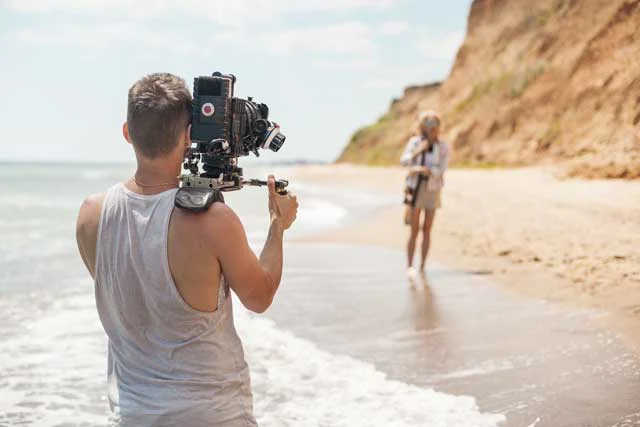 filmmaker with handheld camera shooting on beach on location