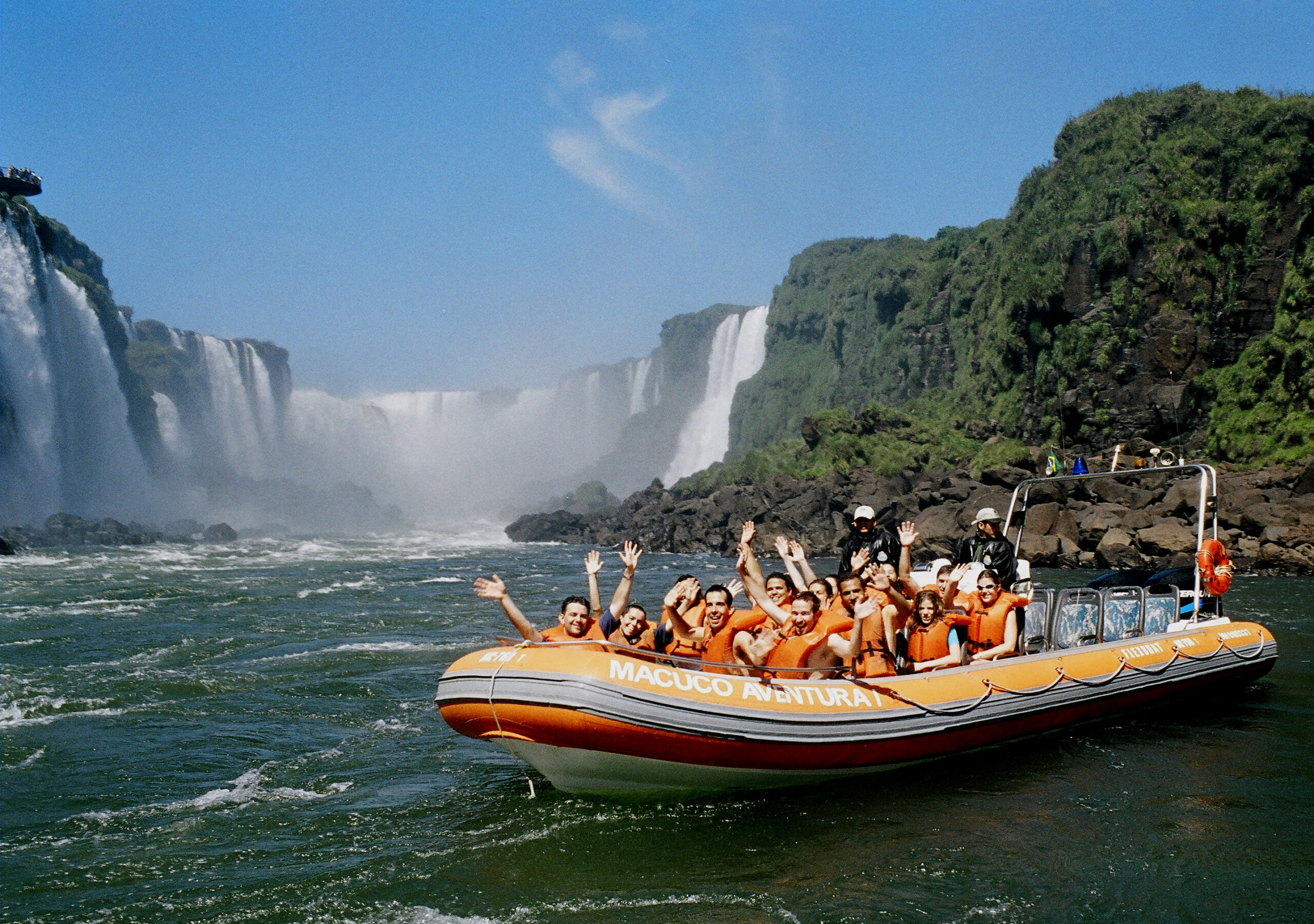 Grupo de turistas em bote inflável do passeio Macuco Safari, usando coletes salva-vidas, navegando próximo às Cataratas do Iguaçu em um dia ensolarado iguassu