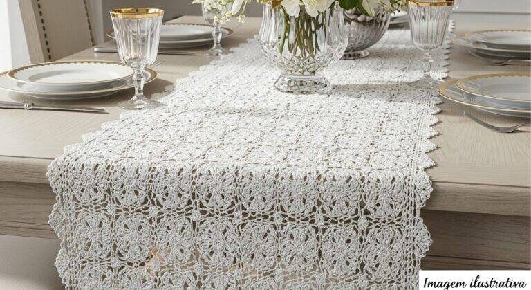 Caminho de mesa de crochê de luxo branco com detalhes dourados sobre mesa elegante de jantar, com a frase “imagem ilustrativa” no canto inferior direito.