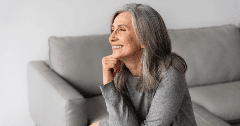 Mulher sorrindo sentada no sofá, transmitindo autoconfiança, serenidade e bem-estar, representando a autoestima equilibrada após os 50 anos.