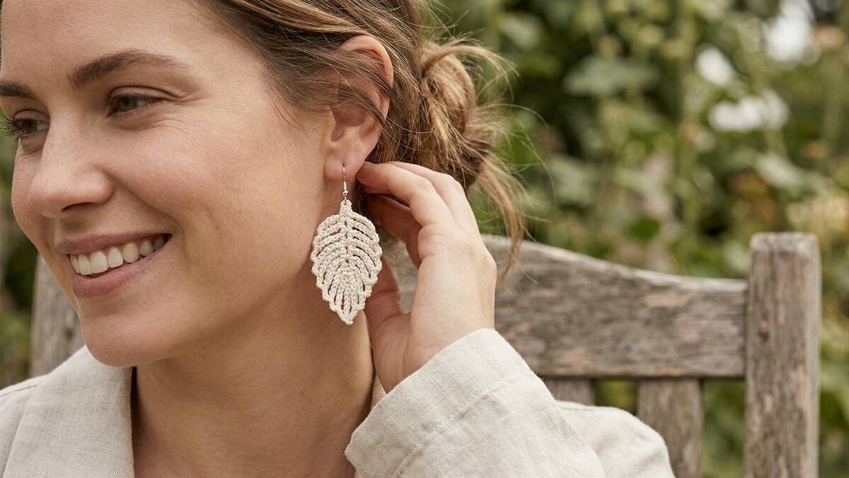 Mulher sorrindo exibindo brincos de crochê em algodão cru, acessórios sustentáveis em ambiente de verão.