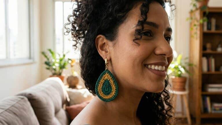 Mulher brasileira sorrindo em ambiente urbano iluminado, usando brincos de crochê em formato de gota nas cores verde esmeralda e mostarda.