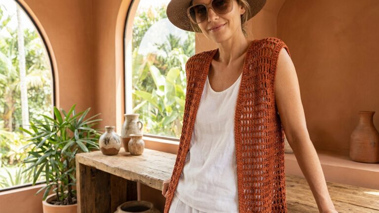 Mulher sorrindo usando colete de croche artesanal terracota leve e arejado sobre regata basica em ambiente iluminado com clima de verao brasileiro
