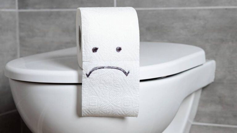 Papel-higiênico com expressão de tristeza desenhada com caneta sobre vaso sanitário