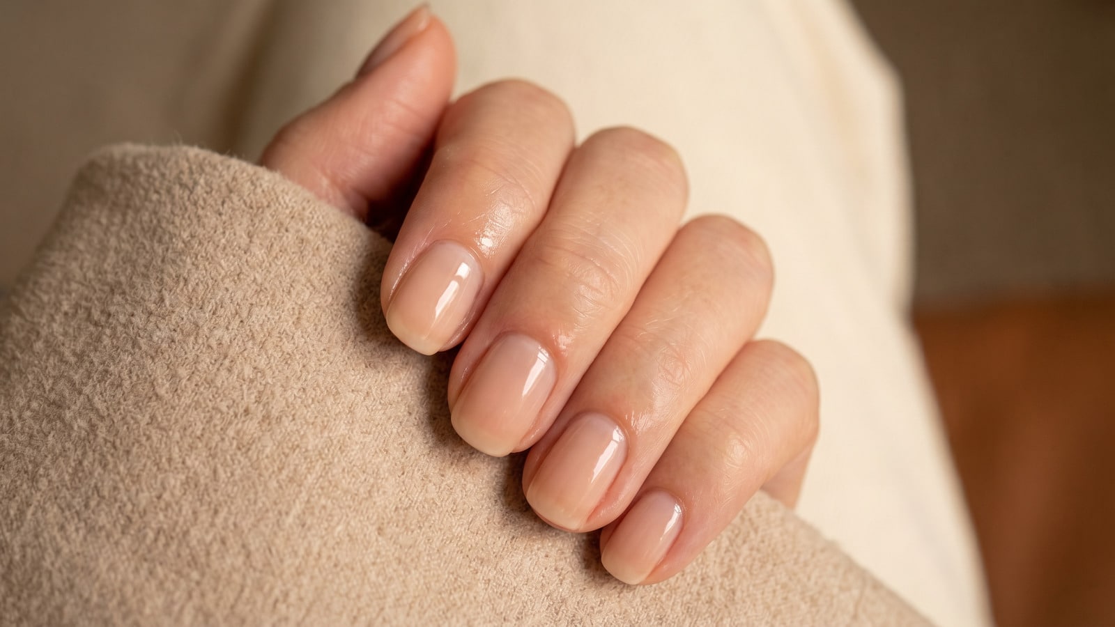 Unhas com esmalte nude translúcido criando efeito natural que disfarça o crescimento.