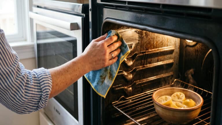 Pessoa limpando forno do fogão facilmente com pano umedecido após aplicação do limão no interior
