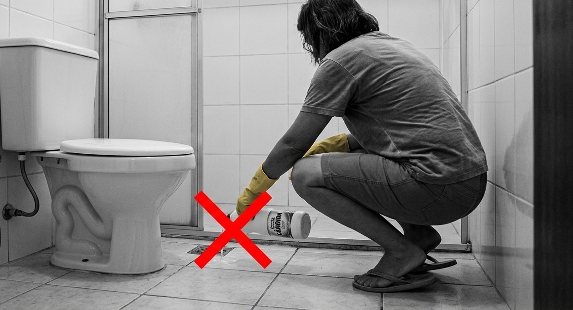 Imagem em preto e branco com detalhes coloridos mostrando uma pessoa agachada com luva amarela despejando água sanitária no piso do banheiro, com um grande "X" vermelho sobre a ação.