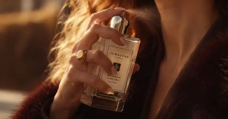 Mulher aplicando o perfume Jo Malone Wood Sage & Sea Salt no pescoço em um close destacando o frasco da fragrância.