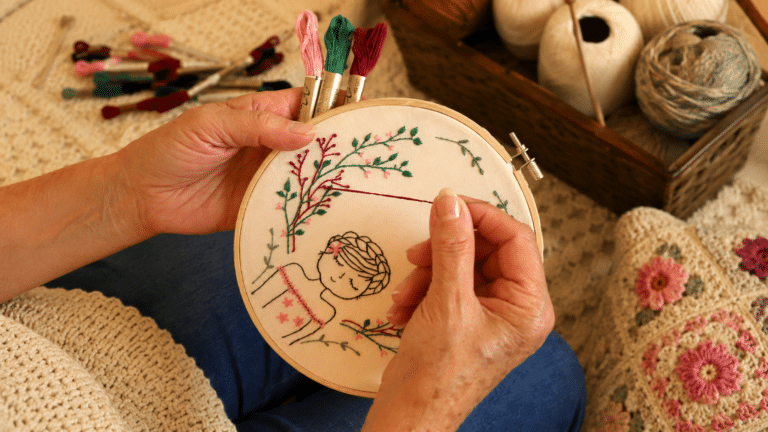 Artesã bordando flores coloridas em um bastidor, celebrando o Dia do Bordado.