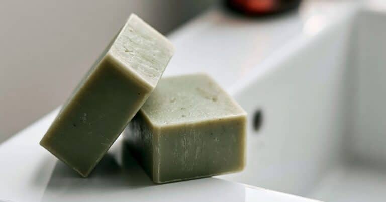 Dois sabonetes artesanais verde menta sobre uma pia branca em banheiro moderno com fundo desfocado.