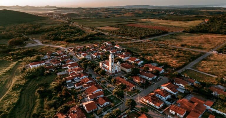 Vista aérea de uma pequena cidade do interior paulista com igreja central, casas e áreas rurais ao redor.