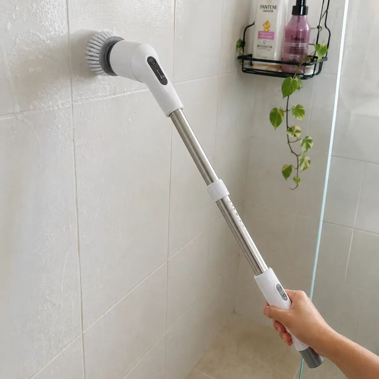 Escova elétrica de limpeza com cabo comprido sendo usada para limpar os azulejos do banheiro.