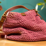 Bolsa de crochê rosa com estrutura deformada, apresentada em ambiente de artesanato, ilustrando como a escolha do fio, da agulha, do ponto e da construção pode influenciar o formato e a resistência da peça.