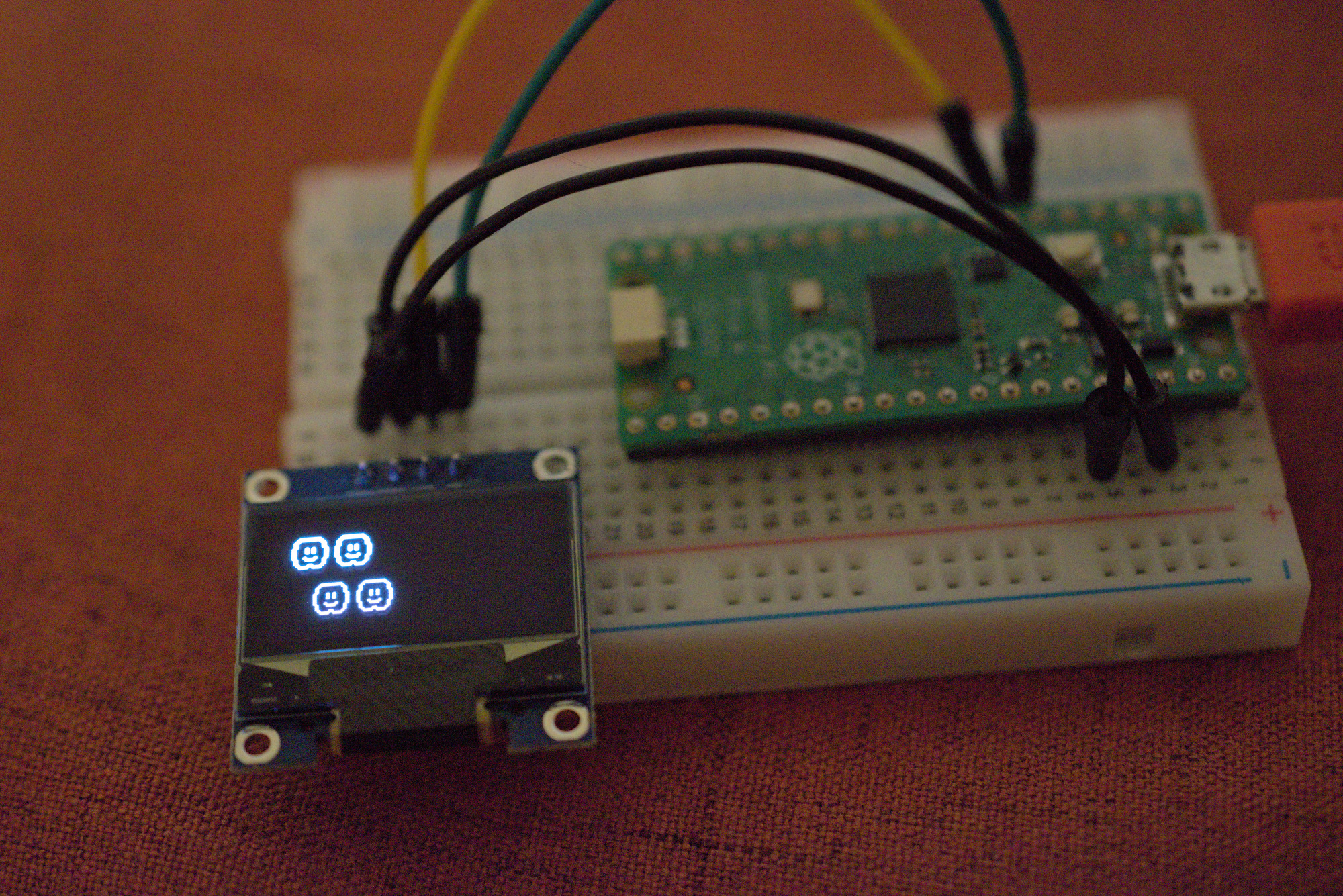 A photograph of the Pi Pico showing four little cloud sprites on the OLED screen. The sprites are from some old Mario game