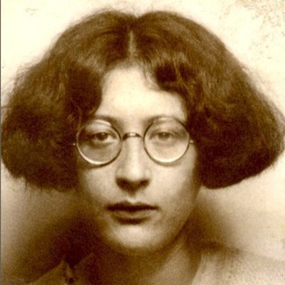 A sepia-toned photo of Simone Weil. She is wearing round glasses and her hair is styled in a short, thick bob. She has an uninterested expression on her face. Photo Credit: Unknown photographer and date. Photo Source: Wikimedia Commons 