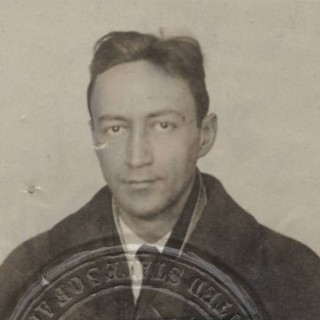 A sepia-toned passport photo of Jean Toomer. He is a light-skinned man with luscious-looing dark hair. He is wearing a coat and scarf while gazing directly into the camera. There is an official-looking stamp silhouette overlaying the bottom 1/3 of the photo.