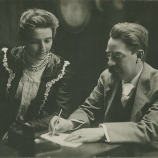 A sepia-toned photograph of Sidney and Beatrice Webb looking at a piece of paper together while Sidney writes something on the paper. c1895. Photo Source: London School of Economics Photo Archive