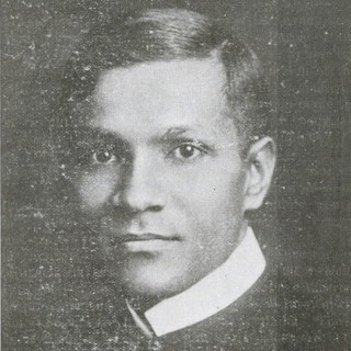 A black and white photo portrait of a young Benoy Kumar Sarkar. His hair is neatly slicked into a side-part and he is looking intensely into the camera.