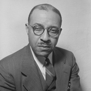 A grayscale photo portrait of Dr. Charles Johnson. He is wearing a well-pressed suit with a tie. He has round glasses and buzz-cut hair. His facial expression appears serious and deep-in-thought. Photographer: Gordon Parks. Created between 1935-1945.