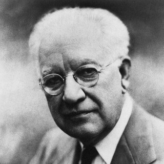 A gray-scale photo portrait of Robert Park. He is wearing a suit and tie. He has round glasses, a clear-shaven face, and white hair. He is looking directly into the camera. Photo Credit: photographer and date unknown.