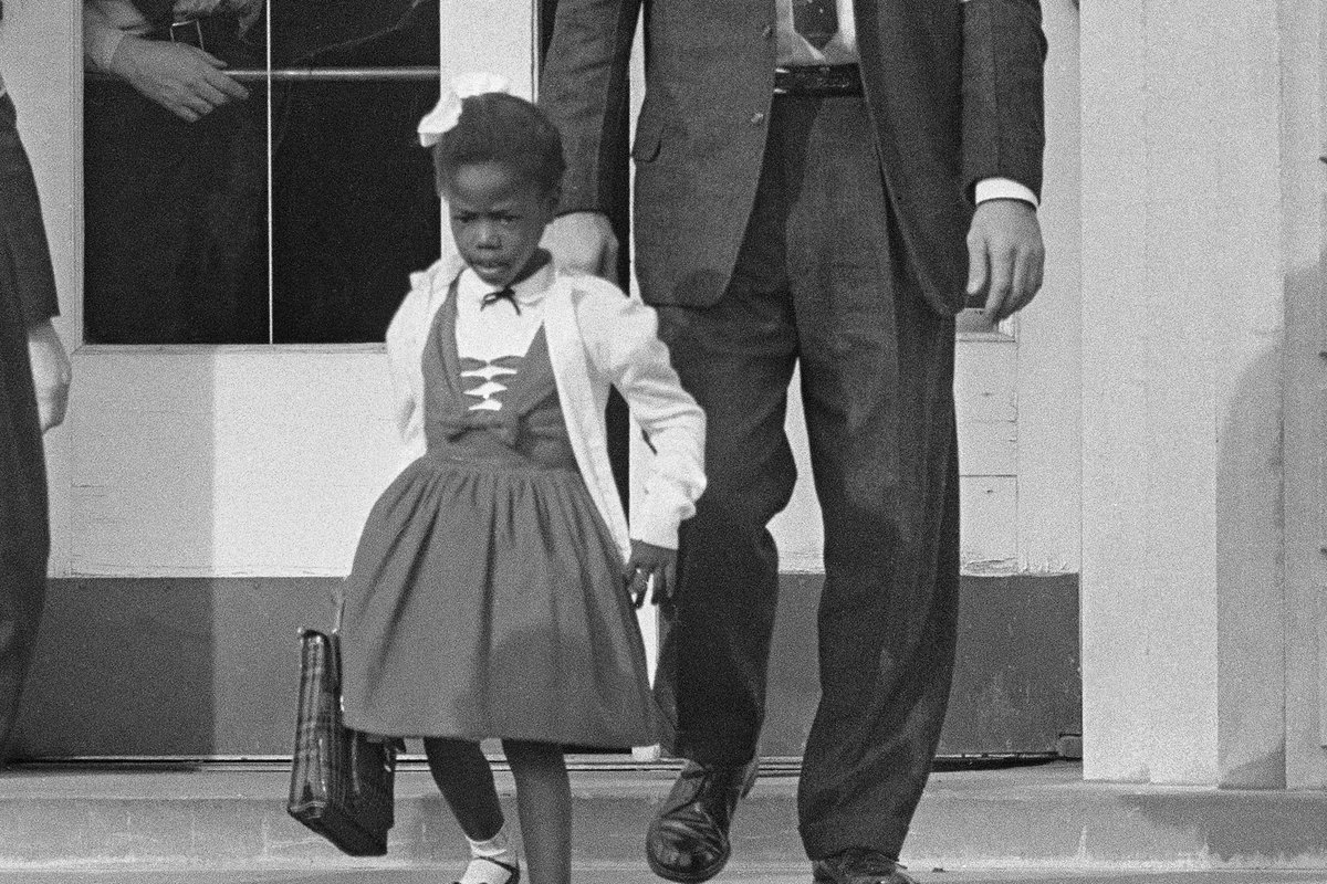 Six-year-old Ruby Bridges, in a white dress, descends school steps escorted by four U.S. Marshals in suits and armbands.
