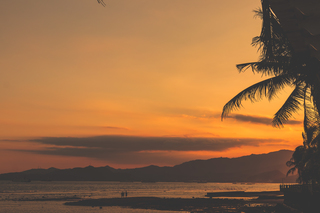 A photograph of a tropical shore with the silhouettes of two people in the foreground.
