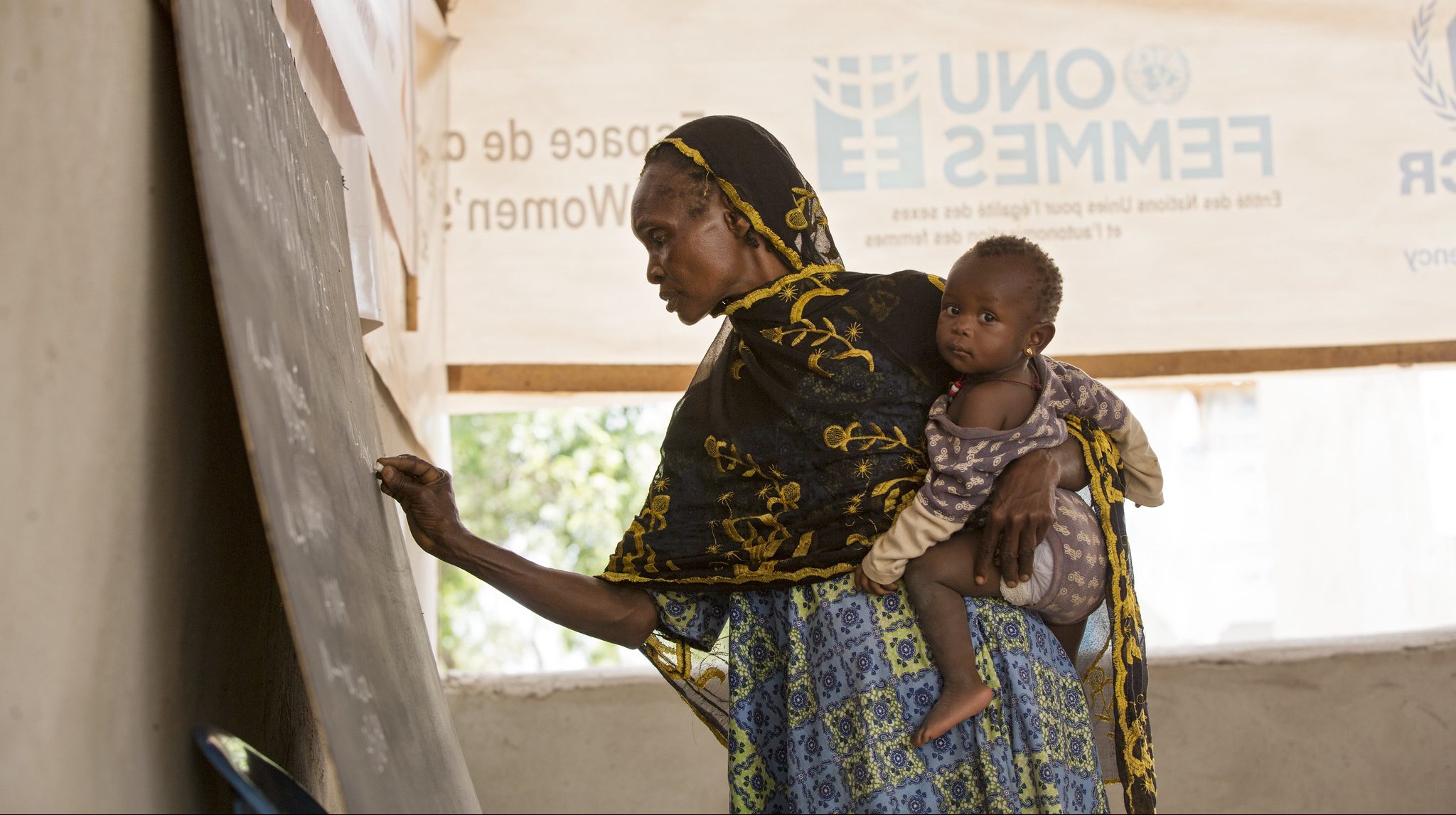 Refugee from Cameroon holds her granddaughter while taking an adult education class