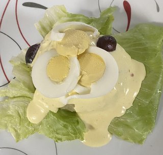 Papa a la Huancaína, a Peruvian dish with cold potato slices and hard-boiled egg slices on a bed of lettuce, covered in a cramy, spicy sauce