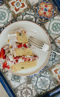 A slice of white cake with 3 layers, filling of chopped strawberries, and white merengue on the outside