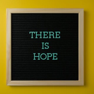 A black sign on a yellow background with the words “There is Hope”.