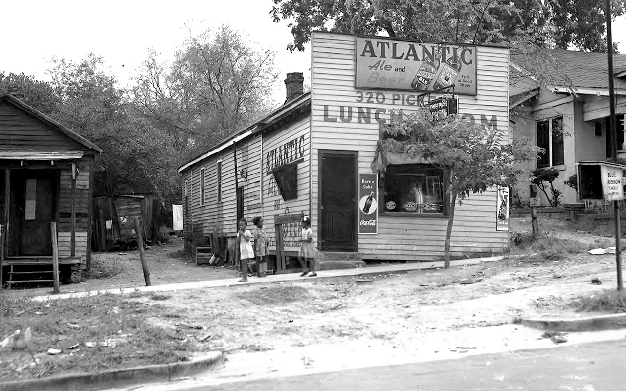 Small town street with convenience store, three young girls socialize in front.
