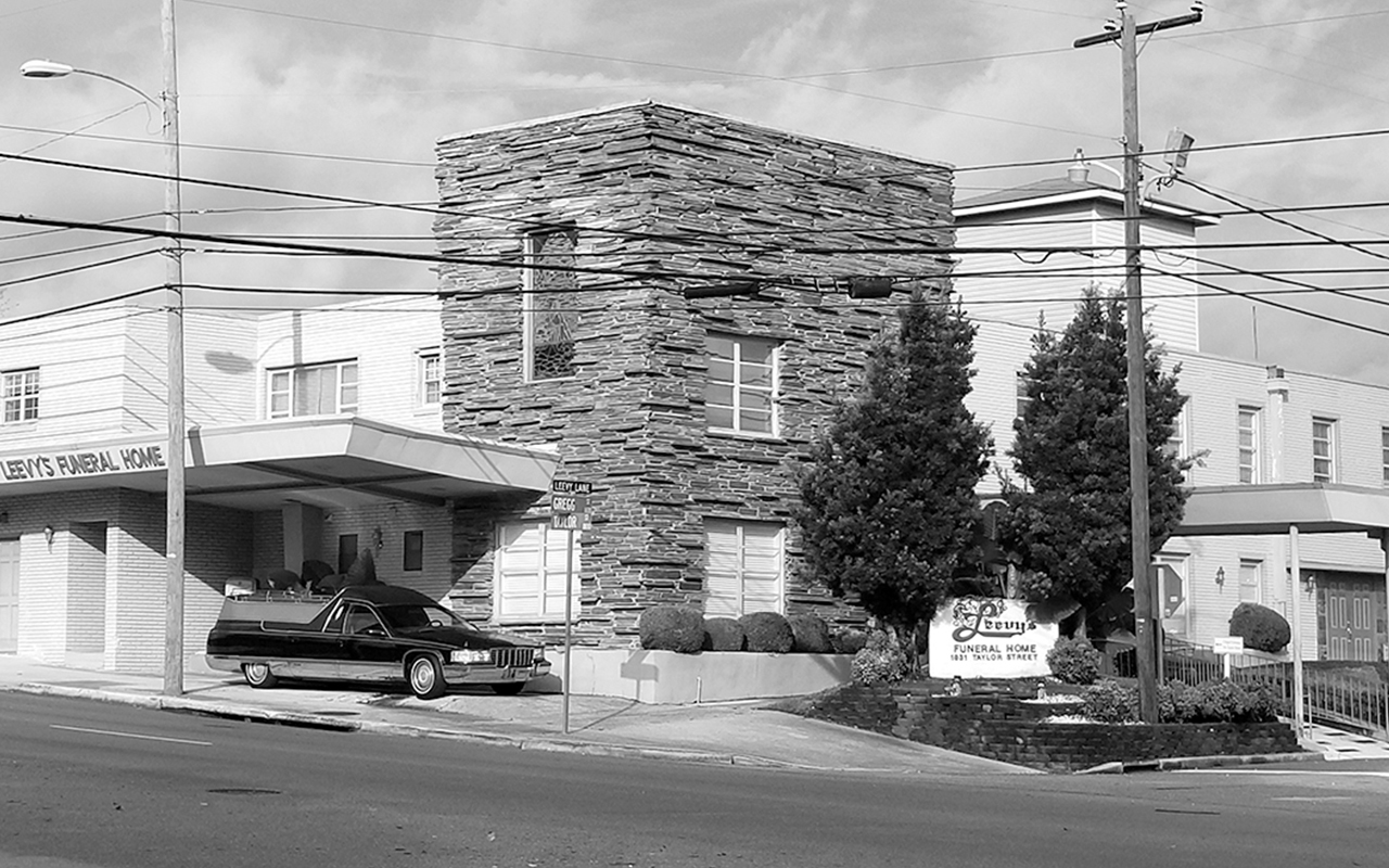 Mid-century modern brick funeral home with hearse parked in front.