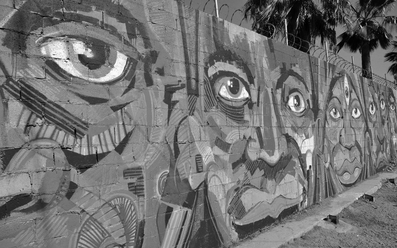 Mural of faces on concrete wall topped with barbed wire.