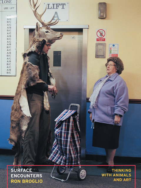 Marcus Coates wearing a deer costume stands near an elevator, speaking to an older woman with a shopping trolley.