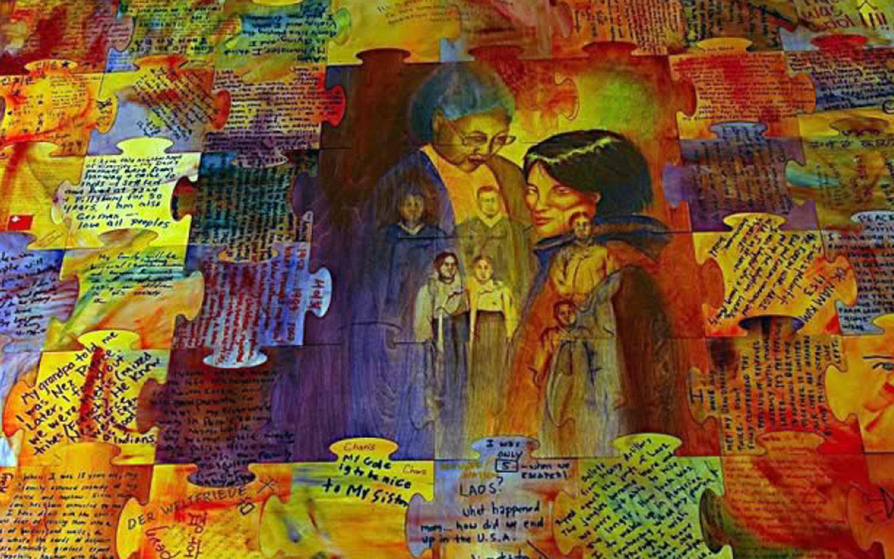 Mural of faces on concrete wall topped with barbed wire.