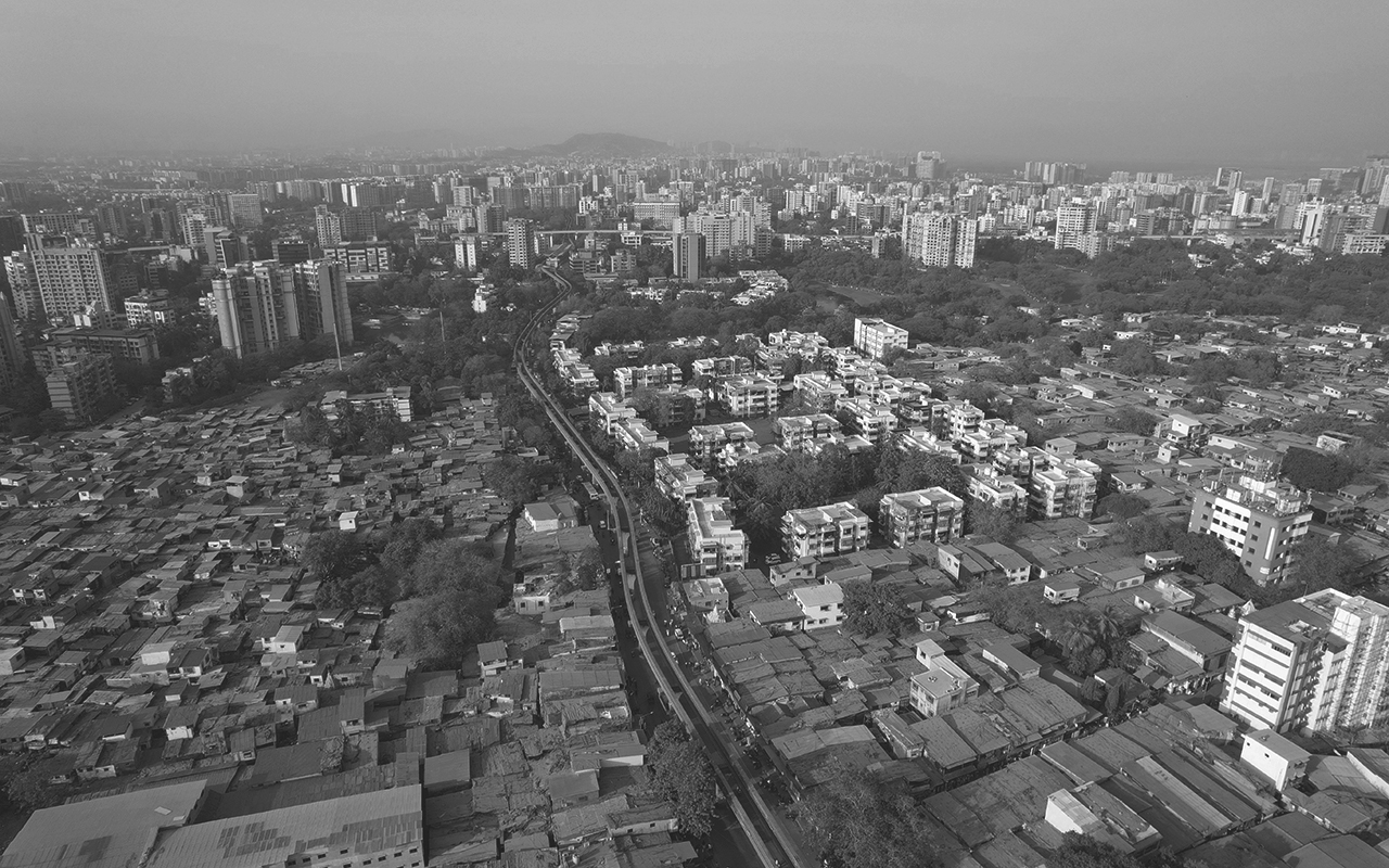 Aerial view of Mumbai showing urban center in the background with smaller buildings in the foreground, trees wending throughout.
