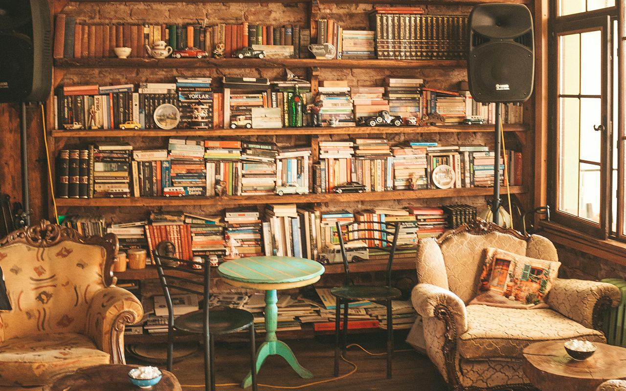 Warmly lit room show two upholstered accent chairs in front of a large library of well-used books. 