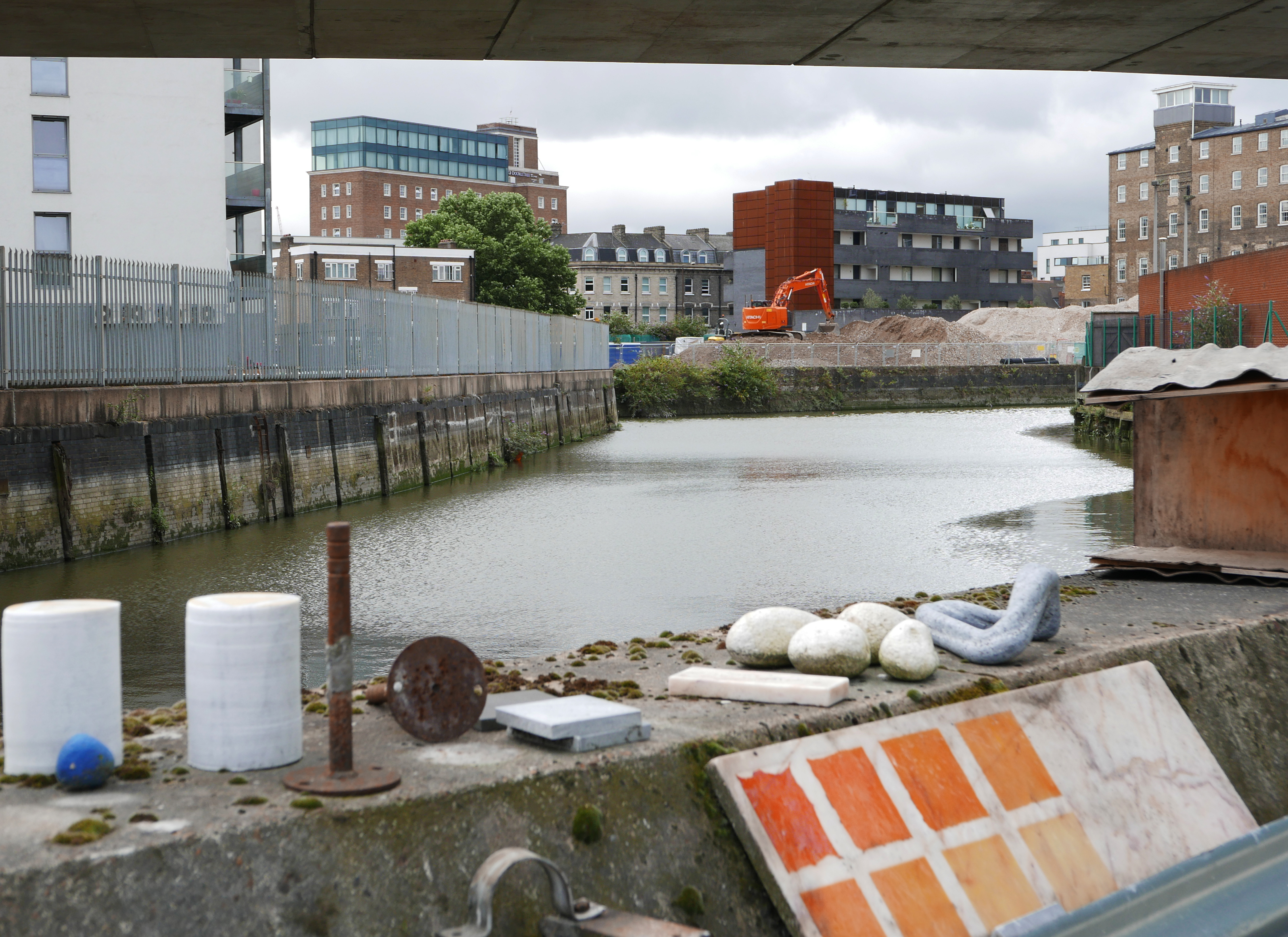 An urban canal cuts through the foreground with a construction site before residential buildings in the background.