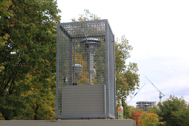 A concrete pedestal supporting a piece of equipment with a vertical tube and top cap is enclosed within metal fencing.