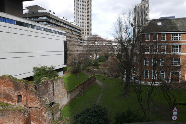 A view looking down onto a green urban courtyard and walkway positioned between newer structures and older brick structures little more than mossy walls.