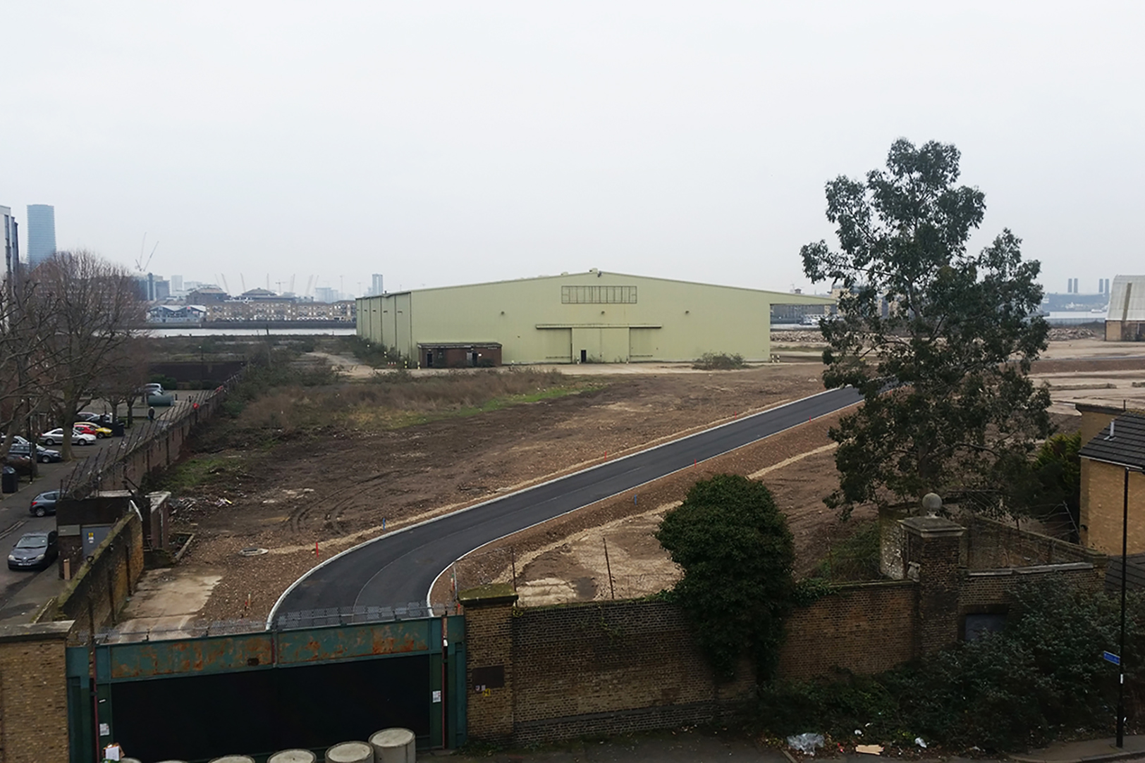 A fenced-in commercial building with green steel siding abutting a river in the background.