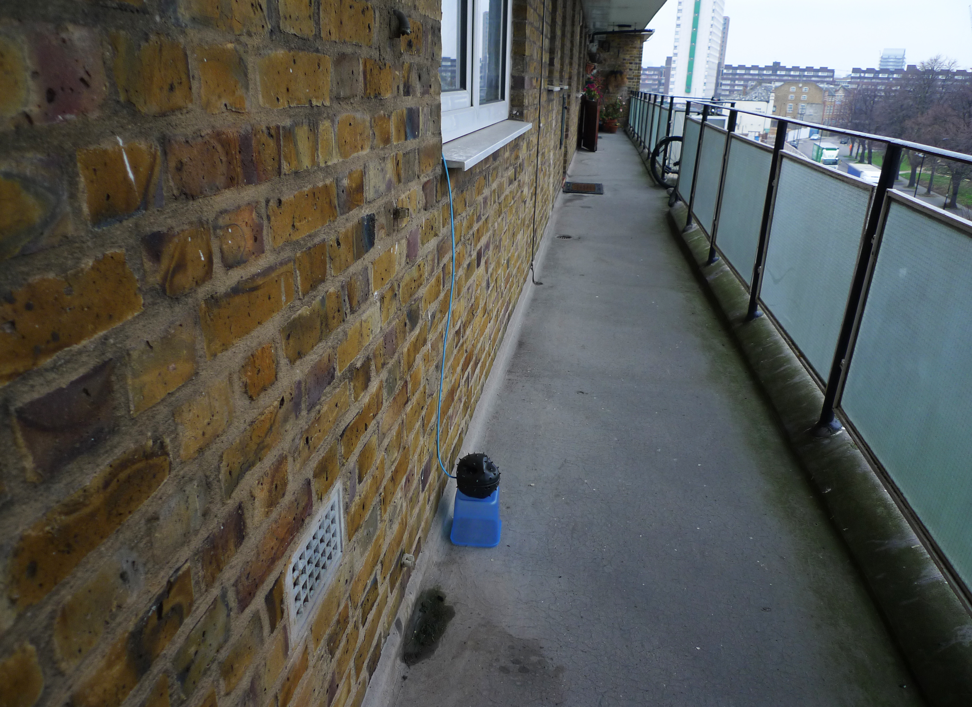 An apartment with a small patio and railing in front of it. A sensor array sits is positioned on the patio below a window, connected by a blue cord.