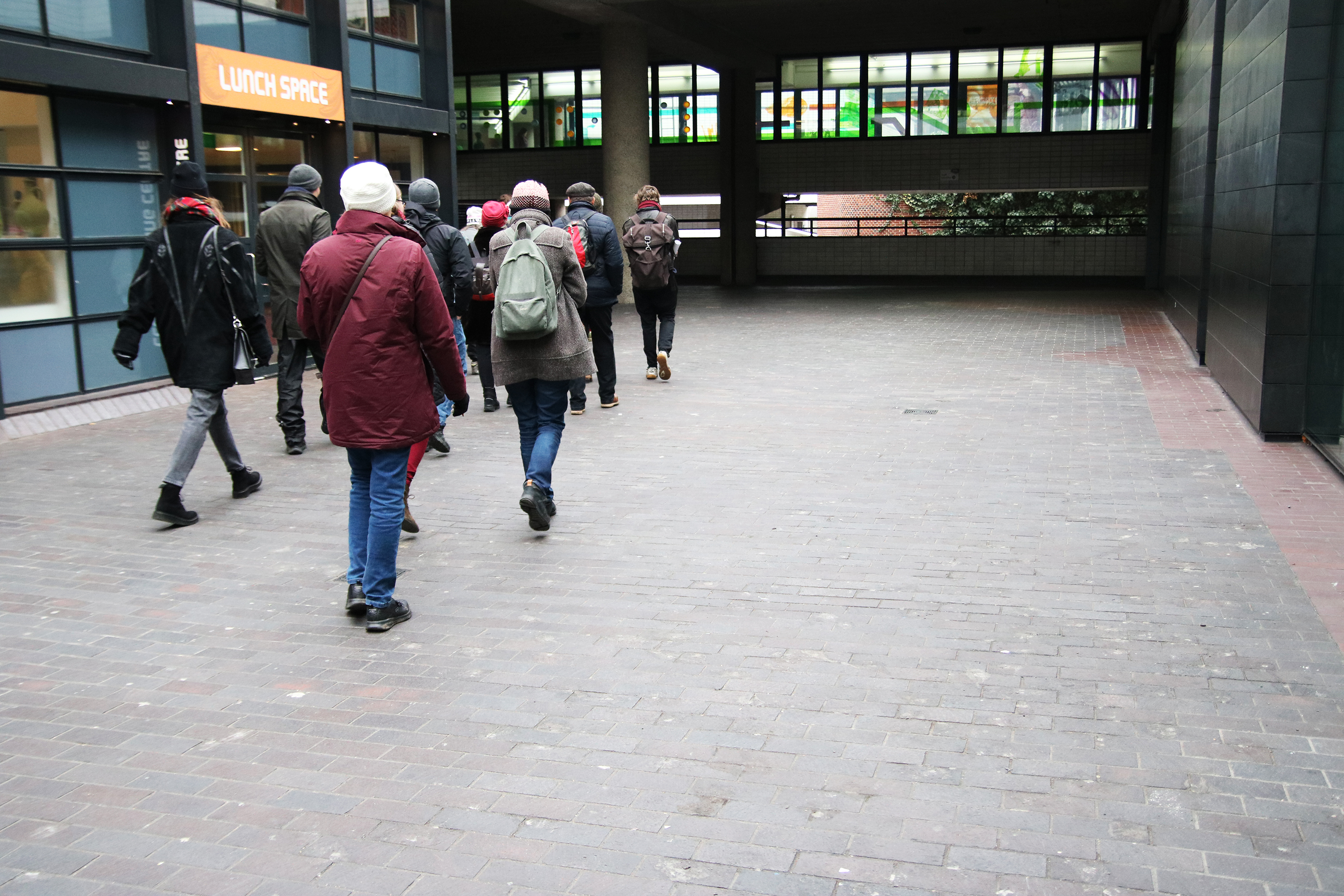A group of people in winter coats walking down a brick courtyard on the ground level of a building complex.