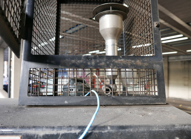 A sensor array with a black, spiny casing positioned within metal gate beside another piece of metal equipment with a topped vertical tube.