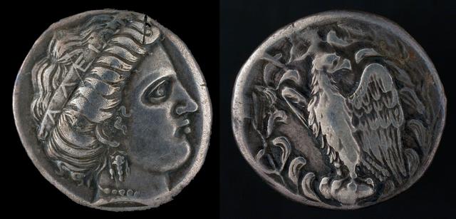 Ancient Greek silver stater from Olympia minted at the Temple of Hera circa 421 BCE. The front side of the coin showcases a profile of Hera adorned with a crown inscribed with "of the Eleains" . The other side displays an eagle.