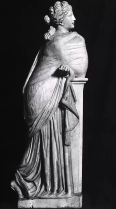 A Roman marble statue of Polyhymnia, the Muse of sacred poetry, standing with her cloak draped over her left shoulder in a contemplative pose. The statue represents Polyhymnia through her serene and thoughtful demeanor. The Muse Polyhymnia statue in the Museo Nacional del Prado in Madrid, Spain is 68 centimeters tall, 51 centimeters wide, and 33 centimeters at the base.